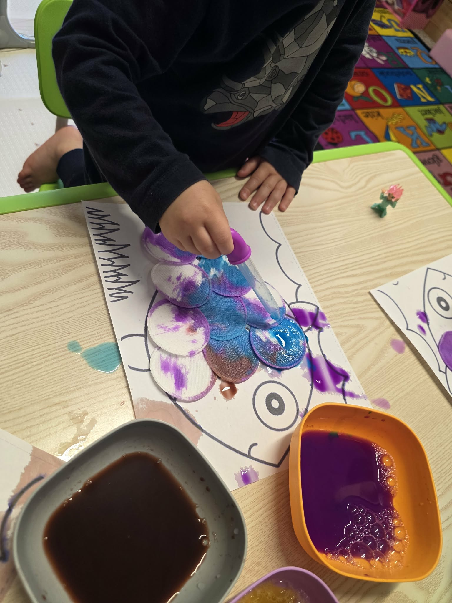 A close-up of a child’s hands adding color to a fish craft with a dropper.