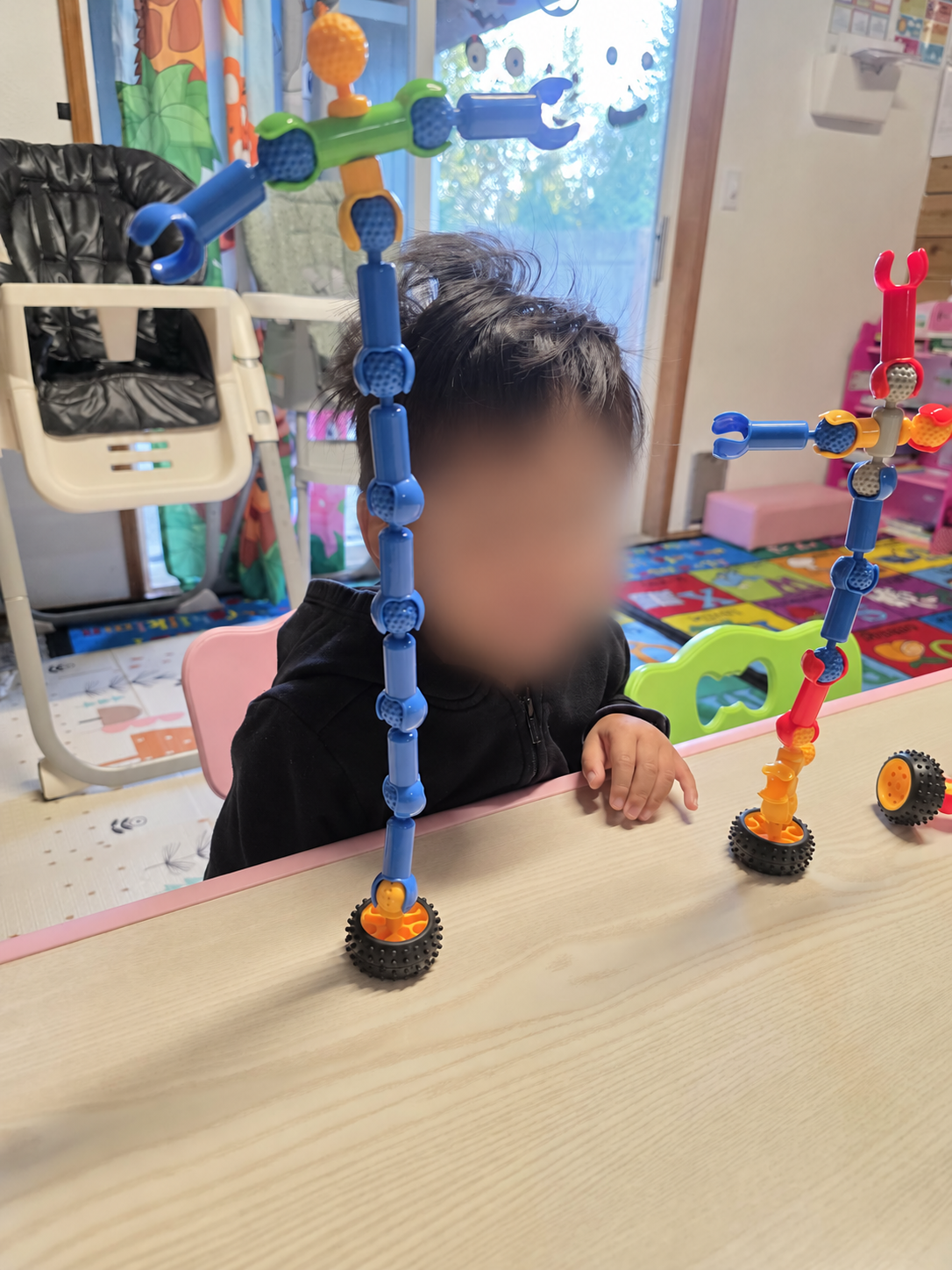 A child building with colorful construction toys, with their face blurred for privacy.